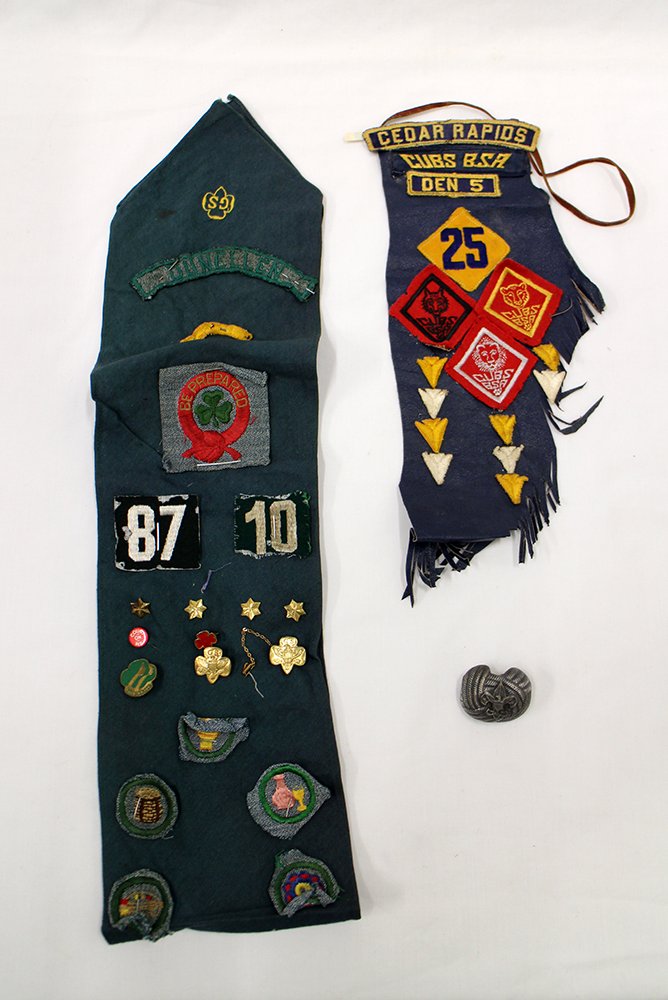 VINTAGE BOY & GIRL SCOUT COLLECTIBLES: Cub scout sash from Cedar Rapids, a Boy Scout neckerchief slide, and a Girl scout sash filled with pens and merit badges.