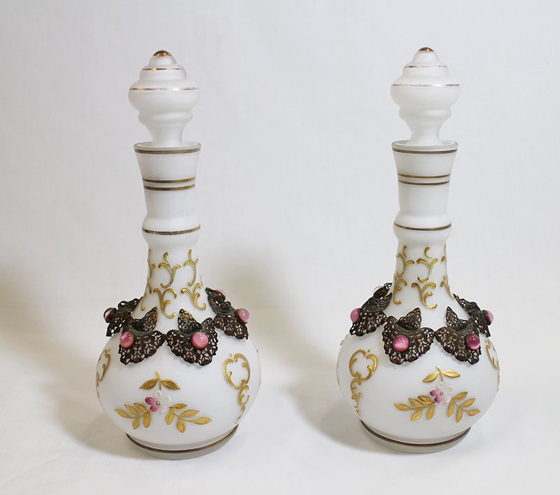 (2) SATIN GLASS JEWELED BOTTLES: Pair of white satin glass bottles. Each is hand painted with flowers and yellow designs. Each bottle has a metal filigree with jeweled star sapphires. 9 1/2" tall.