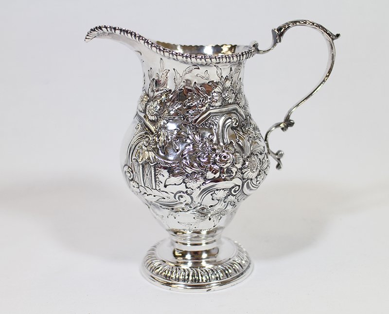 18TH CENTURY STERLING CREAMER: c1765 London hallmarked sterling silver creamer with repousse flower design. Hallmarked with Leopard, Lion, date lower case k, and maker H (cut off by Lion). Measures 5 1/4" tall and weighs 6.17 OZT.