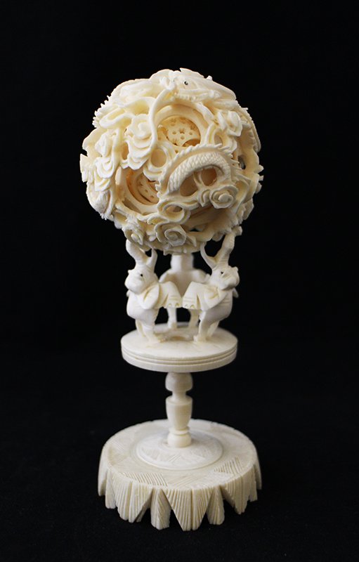CHINESE PUZZLE BALL: Chinese ivory puzzle ball with three elephants on a stand holding the ball. Ball has detailed dragon carvings. Some damage to inside puzzle & one elephant missing part of trunk. 6 1/4" tall. Cannot be