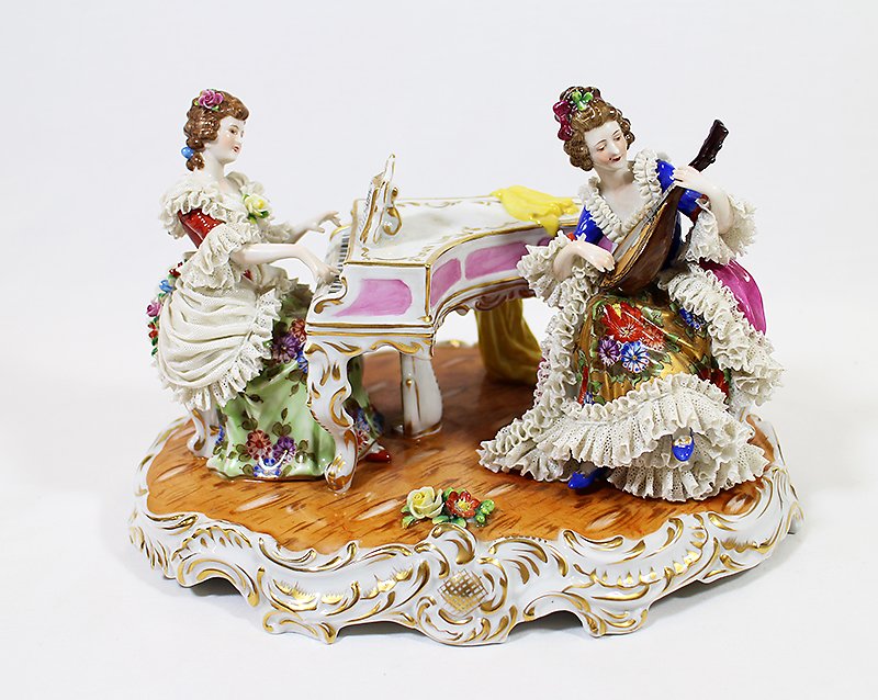 GERMAN PORCELAIN MUSICAL FIGURINE: Porcelain figurine of two ladies, one playing piano and one playing a mandolin. 10" wide 6 1/2" tall. Repair to mandolin and leaf on hair of mandolin player missing.