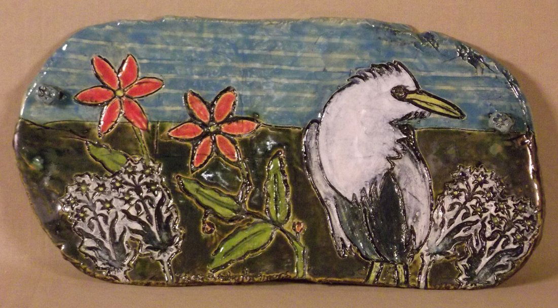 717 - Bodenheimer Sculpture: NIGHT EGRET. Ceramic wall hanging of flowers and bird. Blue, green, orange. Signed in verso. Dated 2012. 8 x 15 in. Donated by Nini Bodenheimer.