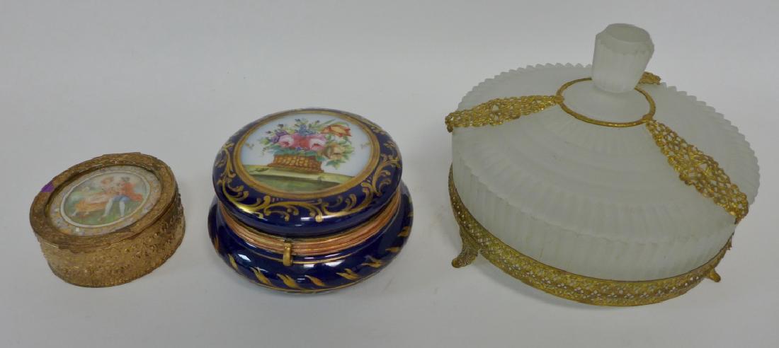 Decorative Round Box Collection: Three assorted decorative boxes. Includes porcelain, glass and gilt metal. Imperfections include chip on bottom of frosted glass box. Height: 6"; Width: 7 1/2"; Depth: 7 1/2". STERLING ASSOCIATES STRI