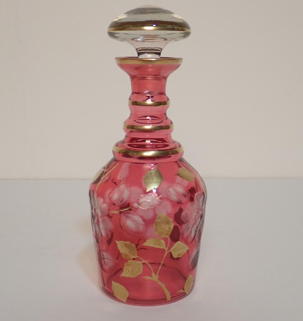 Ruby and Gilted Glass Decanter with Floral Design: Pink Glass Decanter with Gilted Floral Design and Cut Floral Design. Imperfections. Dimensions: 11" H x 3.75" W x 3.75" D. (glass, barware, bar, alcohol, vessel, decorative accessory) STERLING ASSOCIA