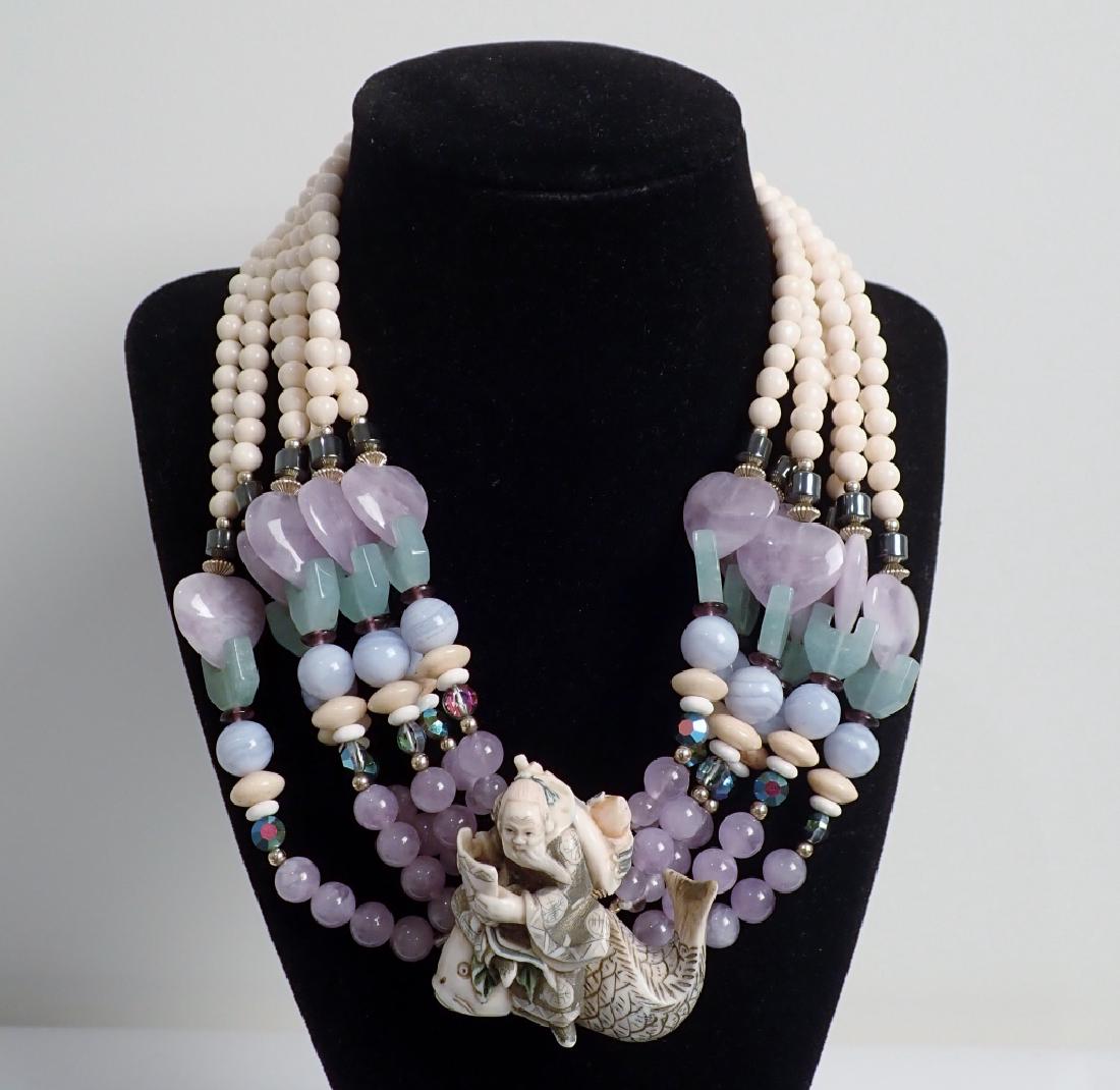 Gemstone Necklace with Carved Netsuke: From the Estate of Joyce Dankoff. Beaded necklace features hand carved Netsuke, Blue lace agate, hematite, Austrian crystal, gold filled beads and more. Possible carved bone. Length clasped: 9 1/2". S