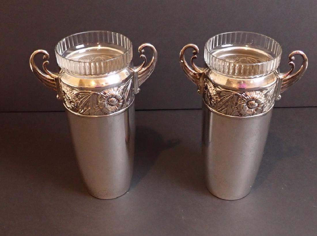 Pair of Art Nouveau Flower Vases: Two matching Double handled urns with glass inserts. Featuring repousse floral art nouveau design border. Makers marks on bottoms ( ALT / 35) Height: 10 1/2"; Width: 6 1/2"; Depth: 4". (Art Deco, vint