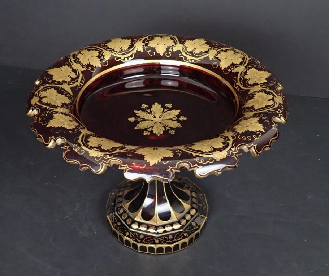 Bohemian Gilt Ruby Glass Compote: Ruby Glass & Gilt Centerpiece / Tazza. Bohemian glass with Scalloped edge, faceted bottom. Height: 8"; Diameter: 11". Imperfections, wear to gilt. STERLING ASSOCIATES STRIVES TO PROVIDE ACCURATE, OBJE