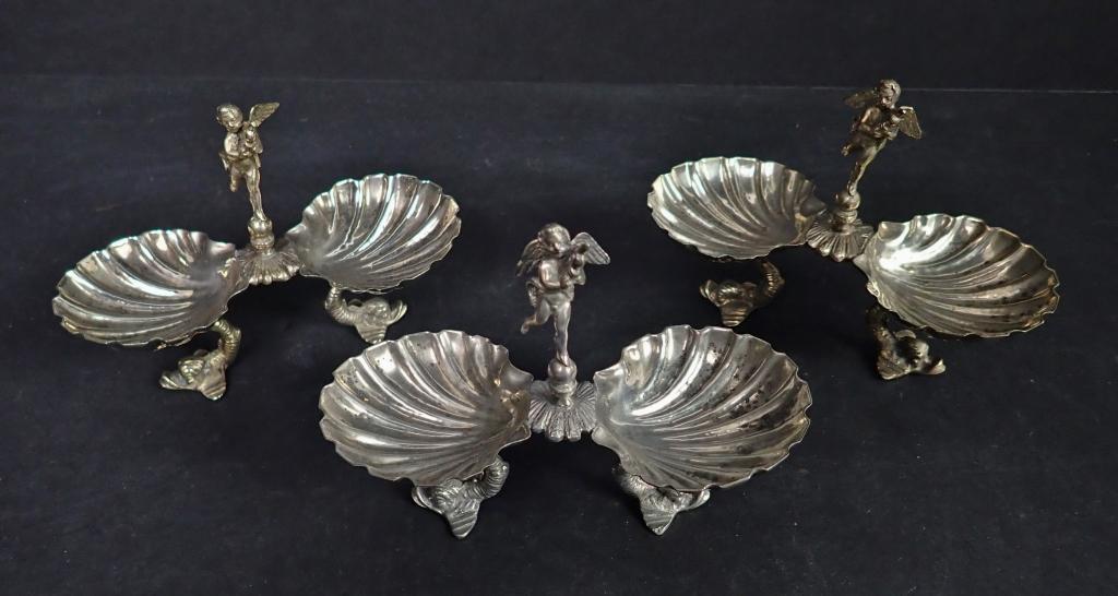 Three 19th C Sterling Silver Figural Salt Cellars: 19th Century Continental Silver Clam & Cherub Salt Cellars. Double clam shell with puti in the center, raised on dolphin shaped legs. Height: 3 1/4"; 4 1/2"; Depth: 2". Total approximate weight: 192 g