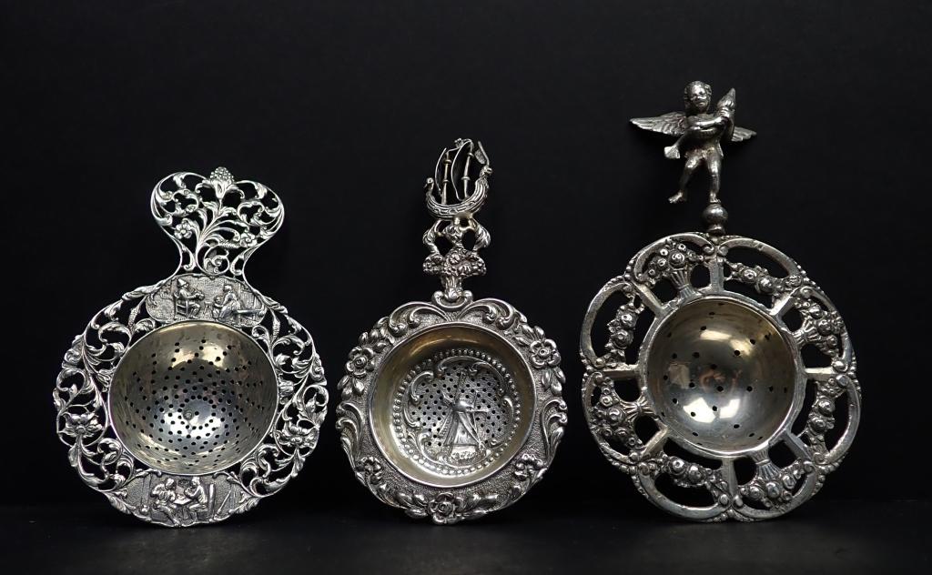 3 Elaborate Figural Silver Tea Strainers: Three Vintage tea strainers. Includes: - Art Nouveau style with figural scenes and floral design. - Long Ship, windmill and floral design. - Winged puti holding a dolphin fish with floral design. Mark