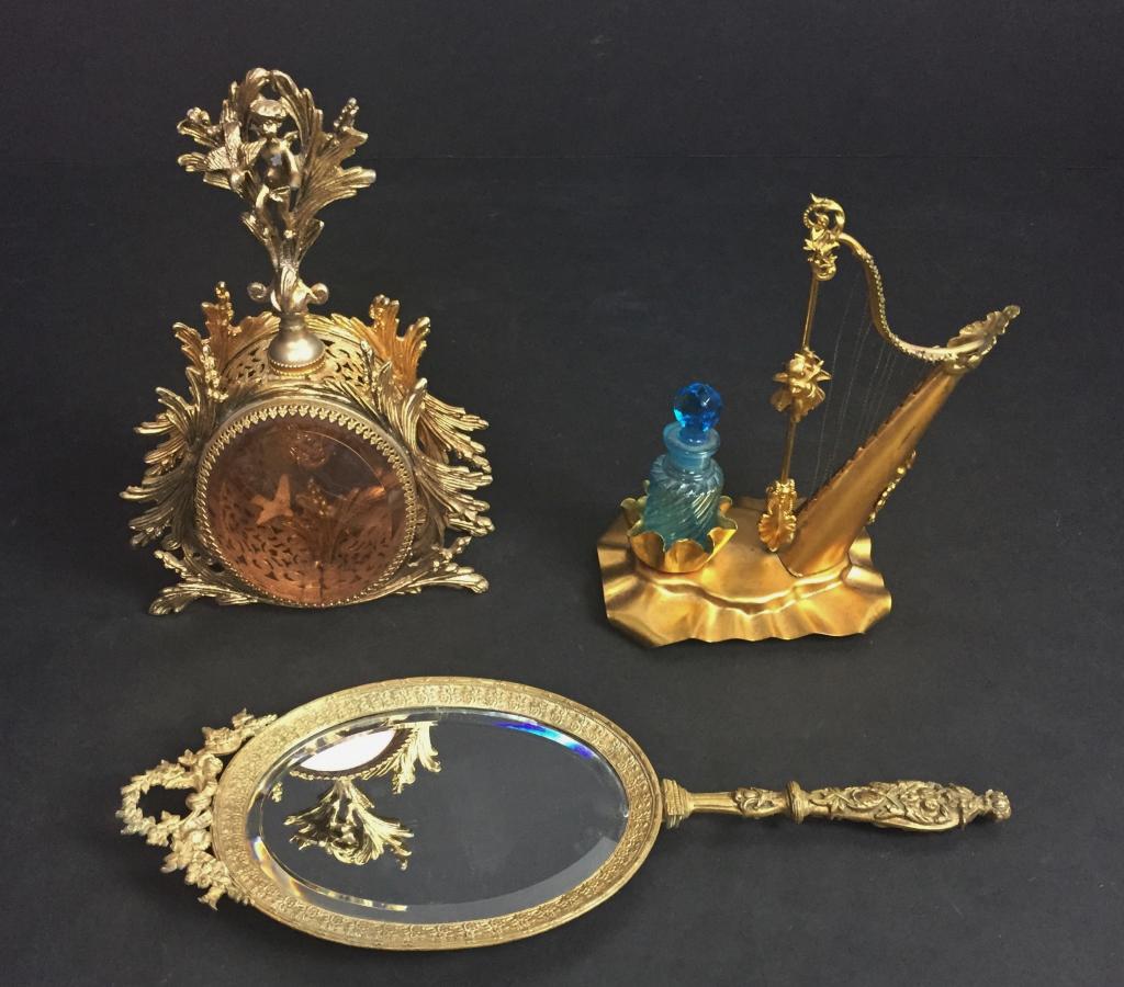 Antique Vanity Assortment: Two perfume bottle holders and a hand mirror. Includes: - Gold Filigree Ormolu Cherub Dove Perfume Bottle. Missing glass insert, loose glass dauber stem. - gilt tin harp perfume bottle holder. Stopper