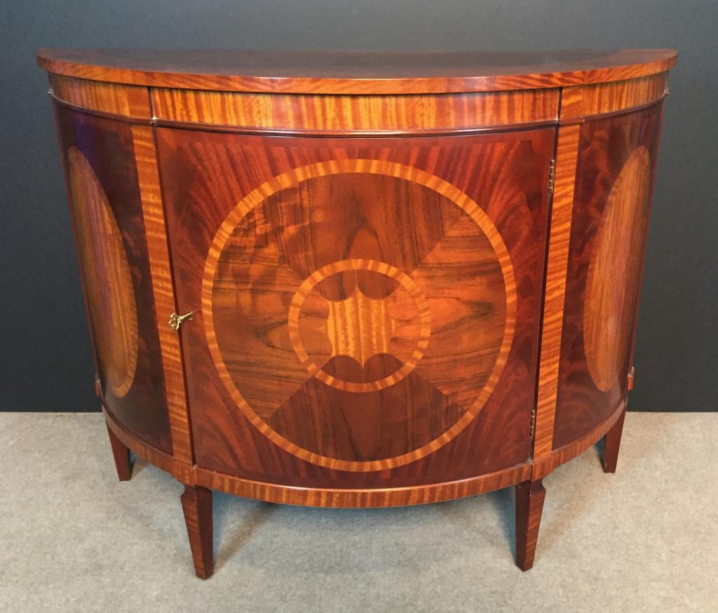 Baker Demilune Side Cabinet: Inlaid Satinwood and Mahogany Demilune Commode. Makers plaques on back read: Historic Charleston Reproductions / Baker Furniture Includes key. Mate is Lot # 81. Height: 37 1/2"; Width: 48"; Depth: 20"
