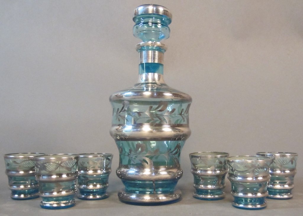 Blue Glass Decanter and Matching Shot Glasses: Blue glass decanter with 6 matching shot glasses, silver enamel floral and striped accents Height: 8 1/2", Width: 3 1/2", Height of cups: 2"