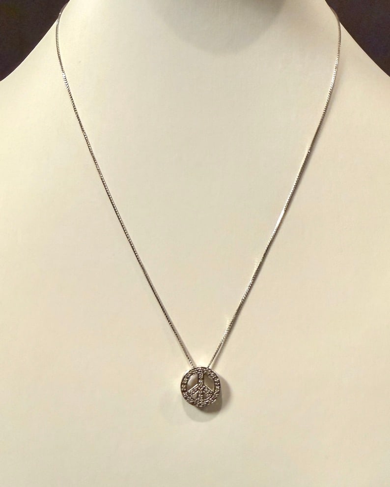 14K White Gold And Diamond Peace Sign Pendant On: Chain Approx. dimensions chain 16". Pendant 1/2" x 1/2". Marked 14K. Approx. gross weight 2.6 grams. STERLING ASSOCIATES STRIVES TO PROVIDE ACCURATE, OBJECTIVE, & FAIR INFORMATION ON ALL LOTS. WE WILL