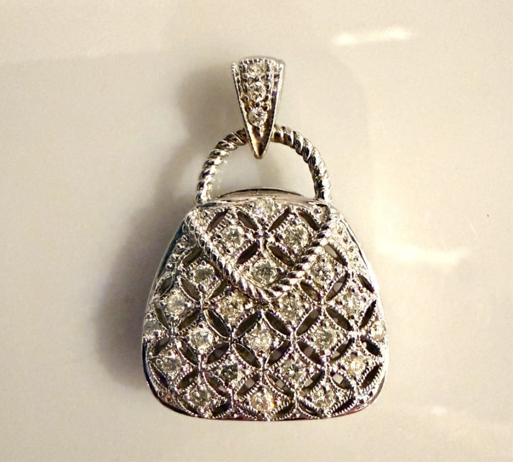 14K White Gold And Diamond Handbag Form Pendant: Approx. dimensions 1" x 3/4" including bail. Tested 14K. Approx. gross weight 7.0 grams. STERLING ASSOCIATES STRIVES TO PROVIDEACCURATE, OBJECTIVE, & FAIR INFORMATION ON ALL LOTS. WE WILL BE HAPPY TO 