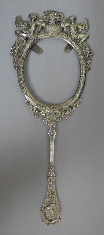 Silver Hand Mirror Case: Heavily decorated figural silver hand mirror case. Hallmark on back tab. Length: 10 1/2". Fits an oval mirror 3 1/8" x 2 1/2". Approx weight: 101 grams.