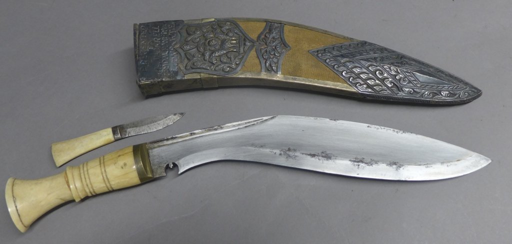 Kukri with Silver Adorned Sheath: Kukri with ivory or bone handle. Sheath is covered in canvas and silver. Features embossed chape (bottom mount), pierced embellishment, shield with lion and locket (top mount) with personalized impres