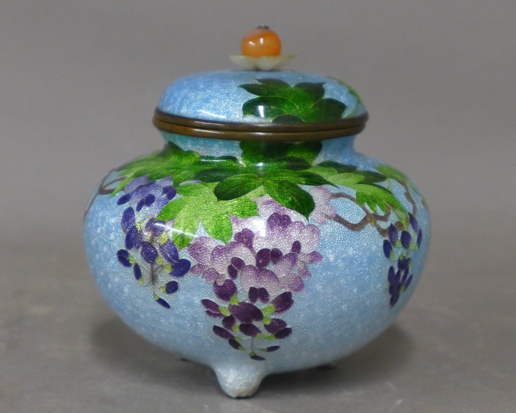 Japanese Cloisonne Vase with Lid: Asian cloisonne enamel spherical box with cover. Beautiful wisteria flowers and leaves on light blue ground. On tripod feet. Orange bead on top of lid. In good overall condition with some wear to bott