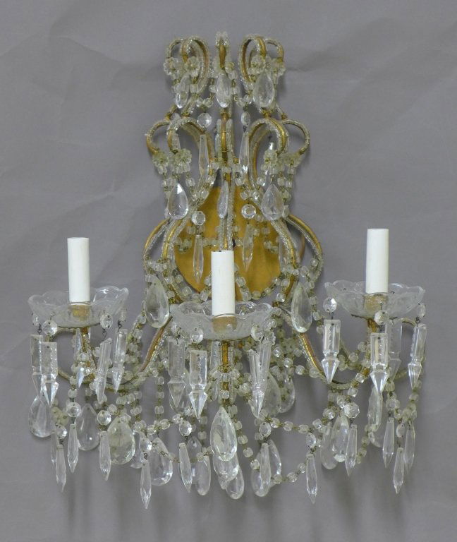 Gilt Iron and Crystal Sconce: Painted metal and crystal sconce with 3 arms/ lights. Scrolled metal frame hung with colorless, beads, swags, rosettes, and prisms. Missing some crystals. Height: 20", Width: 17", Depth: 11" (lighting