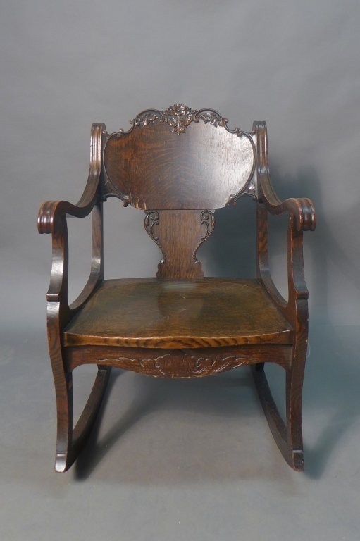 Vintage Victorian Wood Rocker: Vintage wood rocker with scroll shaped arm rests and wide seat. Decorated with carved flower ornament on the back and apron of the seat. Possible repair of the wood veneer at the lower front of the sp
