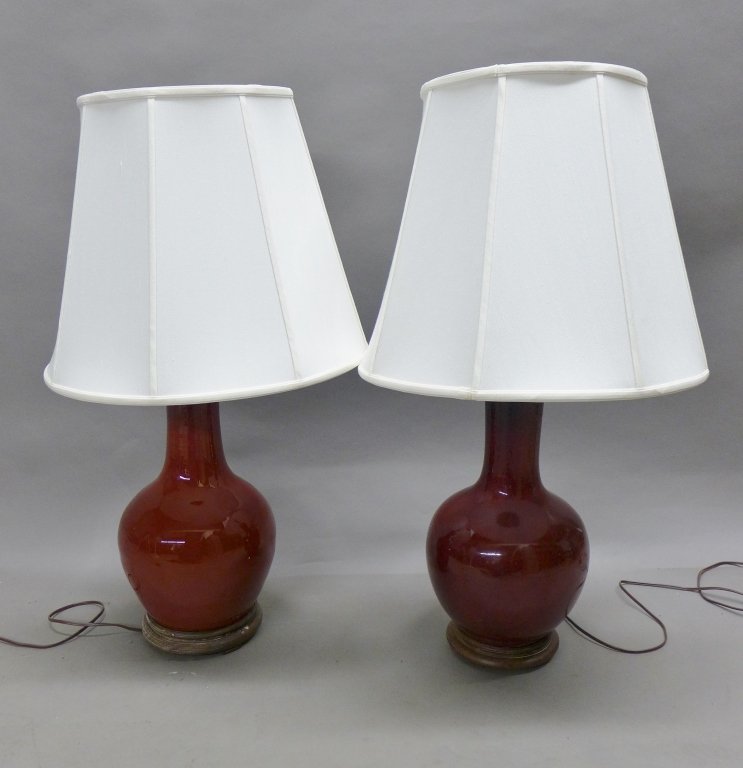 Oxblood Table Lamps: Pair of Chinese oxblood lamps. With large white shades. Wood vase cap and base. Imperfections and noticeable repairs. Height to socket: 22\\\", Diameter: 9\\\"(lighting, electrical, ceramic, pottery, 
