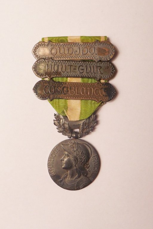 Silver Medal for Morocco (Mdaille de Maroc) 1909: Circular silver medal on laterally-pierced loop and suspension bar with two olive palms supporting a crescent; the face with an oak-crowned helmeted female head facing left representing the French Rep