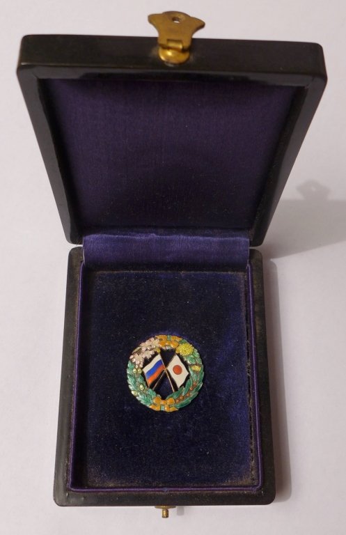Japanese - Russian Society Pin 1910: Japanese - Russian Society pin in an original box. JRS was founded in Tokyo in 1902 by Ryohei Uchida and Ando Kensuke. Featuring vivid colored enamel depiction Russian and Japanese flags crossing, wit