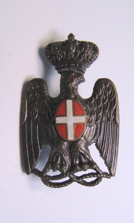 Rare Italian African Police Cap Badge: Rare Italian African Police Cap Badge. The badge is in the shape of an eagle with a crown and red and white enameled central piece. The two fasteners on the back have been lost but both studs are inta