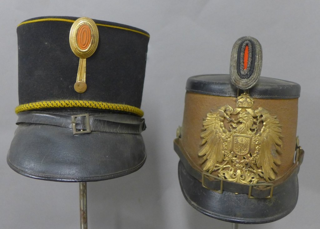 Two Shako Military Caps: Two antique military Shako hats, late 19th century. First brown and black hat has gilt cap badge and officer feldzeichen. Second black hat has gold rope trim, metal feldzeichen and maker's label on th