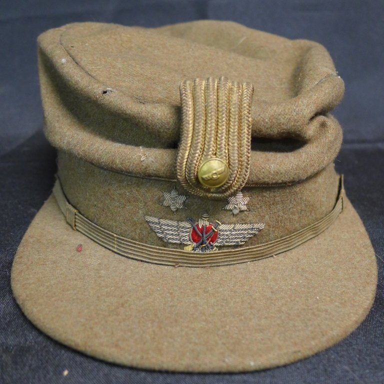 Vintage Military Hat: Embroidered image of two stars, crossed weapons and wings in center. Brass button above embroidery appears to have a similar design. Inside label reads: Trasobares Zaragoza. "MM" pierced in brown leat
