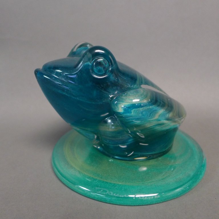 Daum France Crystal Frog On Lily Pad: Stylized frog sculpture and accompanying lily pad. Both are beautiful swirled green and blue glass. Signed on bottom side: Daum France. Height: 3 1/8", Width: 4 1/2", Depth: 4 3/4" & Diameter of lily 