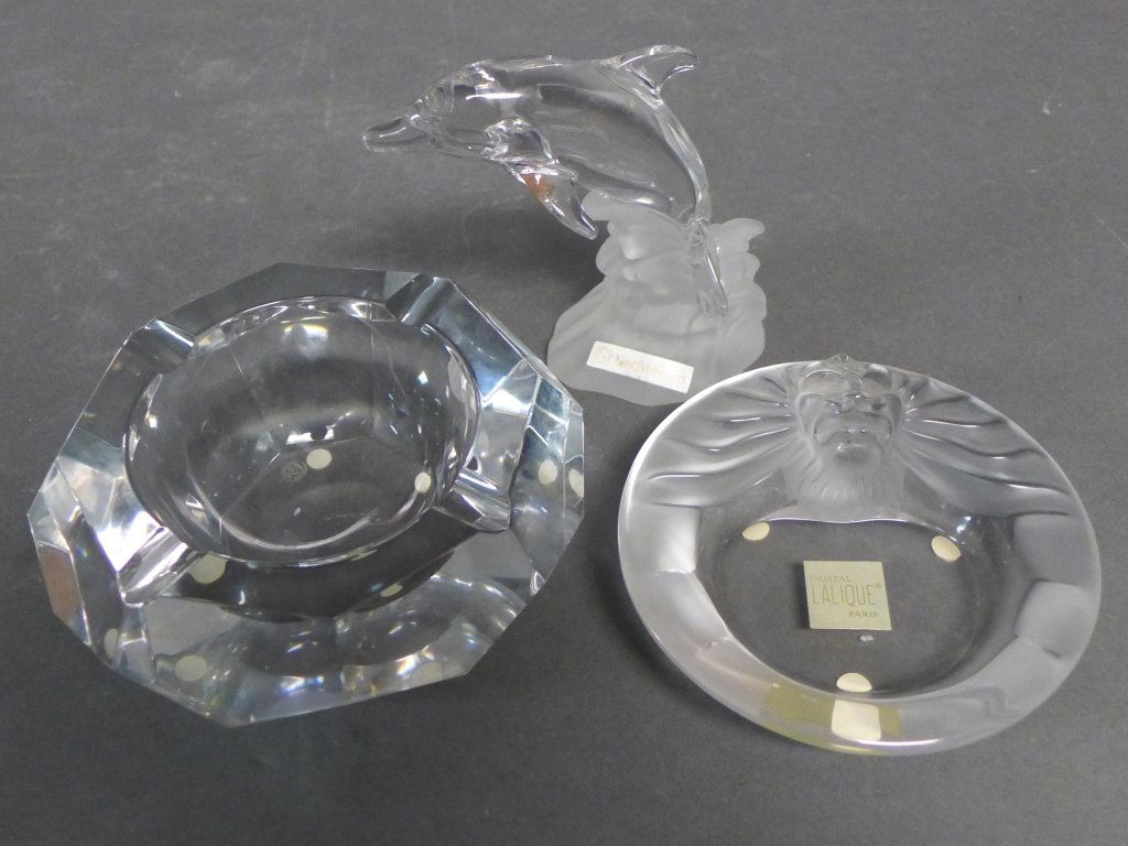 Crystal Grouping: Collection of 3 elegant table top accessories. Lalique Crystal, "Tete de Lion" Ashtray/ trinket dish, French. Together with a Baccarat colorless glass ashtray and a Nachtmann figure of a dolphin. Mino
