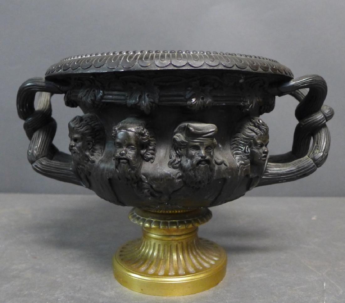 Antique Patinated Bronze Centerpiece Warwick Vase: Grand Tour patinated bronze double handle centerpiece urn. Decorated with sculpted heads, vines and leaves. No noticeable maker's mark. Some wear. Height: 6 3/4", Width: 11", Length: 8" (Campana urn,