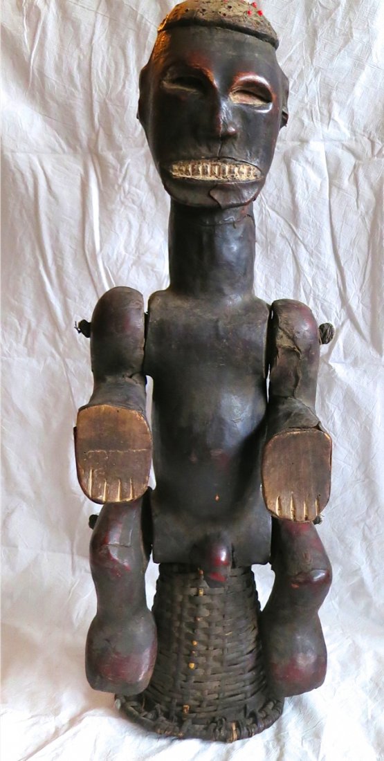 Antique African Carved Statue: Medium: Carved wood, skin covered with articulated legs and arms. Dimension: 29" hgt. This male statue is sitting on an (up-side-down) basket. Inside of the underside of the basket is the location of 