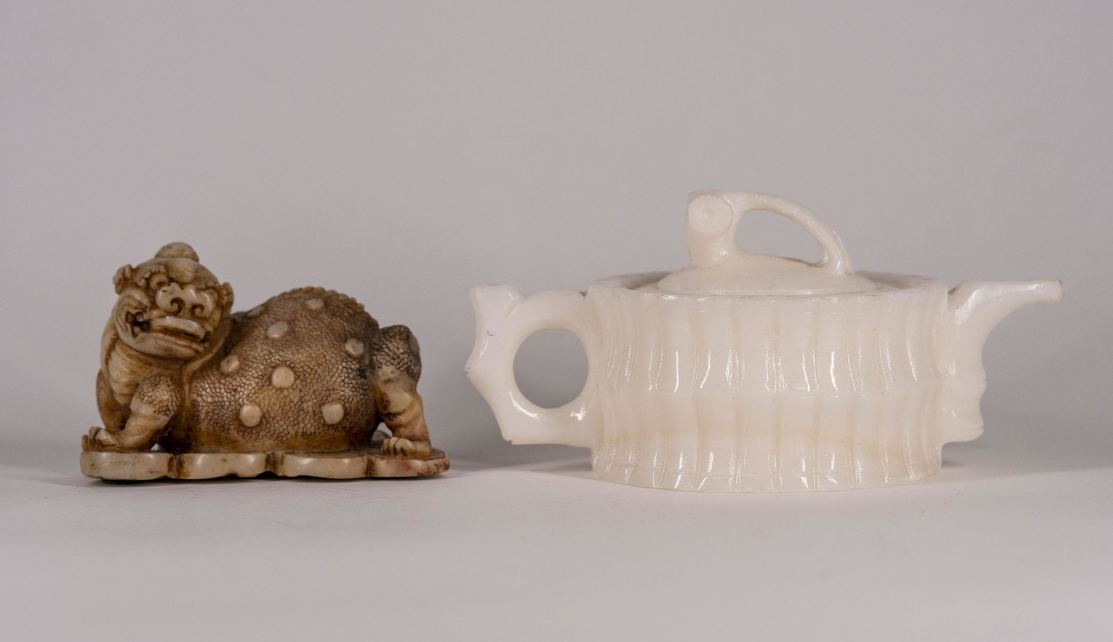 Chinese Carved Hardstone Pi Xiu and Teapot: Reclining Pi Xiu and a white alabaster covered teapot, the sides carved as stalks of tied bamboo. (2) Pi Xiu, H. 2 3/4 in., L. 4 1/4 in., teapot, D. of body 4 in. Note:; pinyin: píxiu or Pi Yao, 