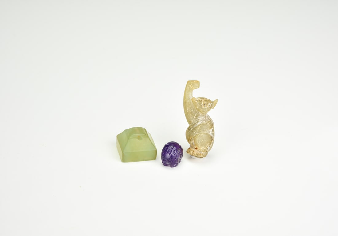 A Group Of Three Hardstone Carvings: Two Beasts And A Seal: A Group Of Three Hardstone Carvings: Two Beasts And A Seal Comprising:1, A celadon jade recumbent beast, well-modeled with raised forepaw and alert head, the stone with russet patches and soft polish.