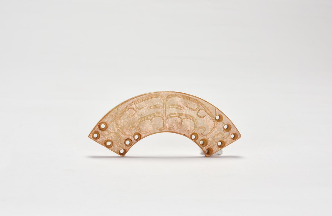 A Carved Jade Crescent Pendant with Dragon Motifs (Huang) Western Zhou Dynasty, ca. 11th–8th: The jade is of warm yellowish-brown tone with natural surface alteration and weathering. Finely carved in the form of a crescent-shaped huang, gently arched and pierced with multiple perforations alon