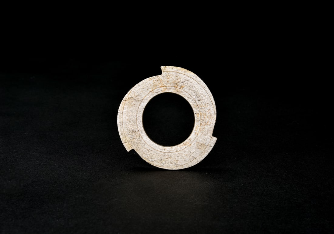Han Dynasty. A Jade Xuanji.: Of circular flattened form with a central aperture, the outer rim carved with symmetrical notches. The outer band incised with stylized cloud scrolls bordered by raised string lines. The stone extensi