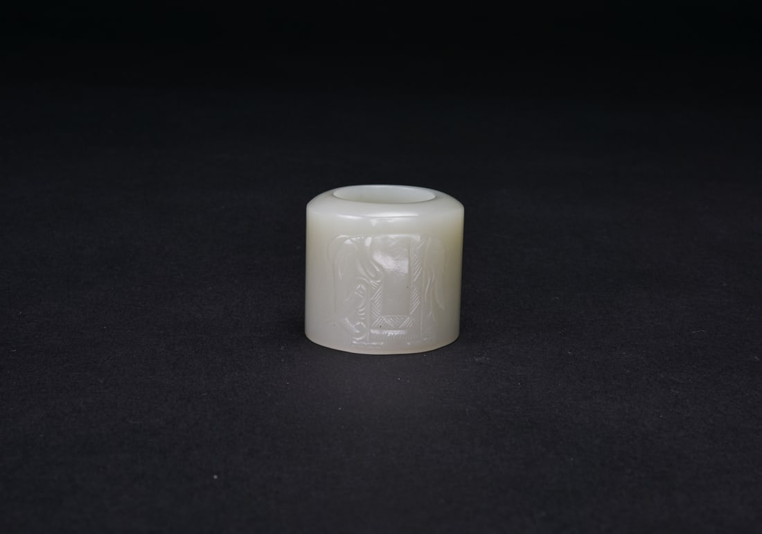 A White Jade Carved Elephant Archer Ring.: Of white jade. The exterior carved in low relief with an elephant motif.H: 1 1/4 In (3.2 cm) D: 1 3/8 In (3.5 cm)清-白玉刻象圖班指白玉ท