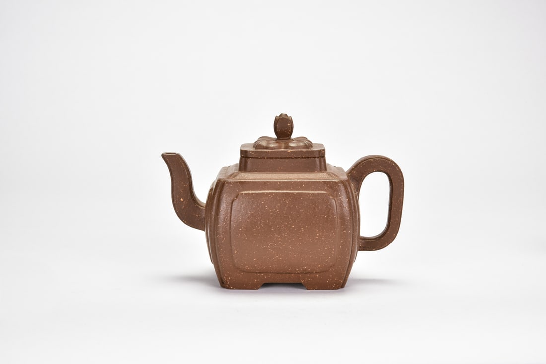 A Yixing Stoneware Square Teapot, Signed Youquan: Of compressed square section with gently rounded corners, raised on a stepped foot and set with a canted spout opposite a rectangular loop handle, the domed square cover surmounted by a lotus-bud fini