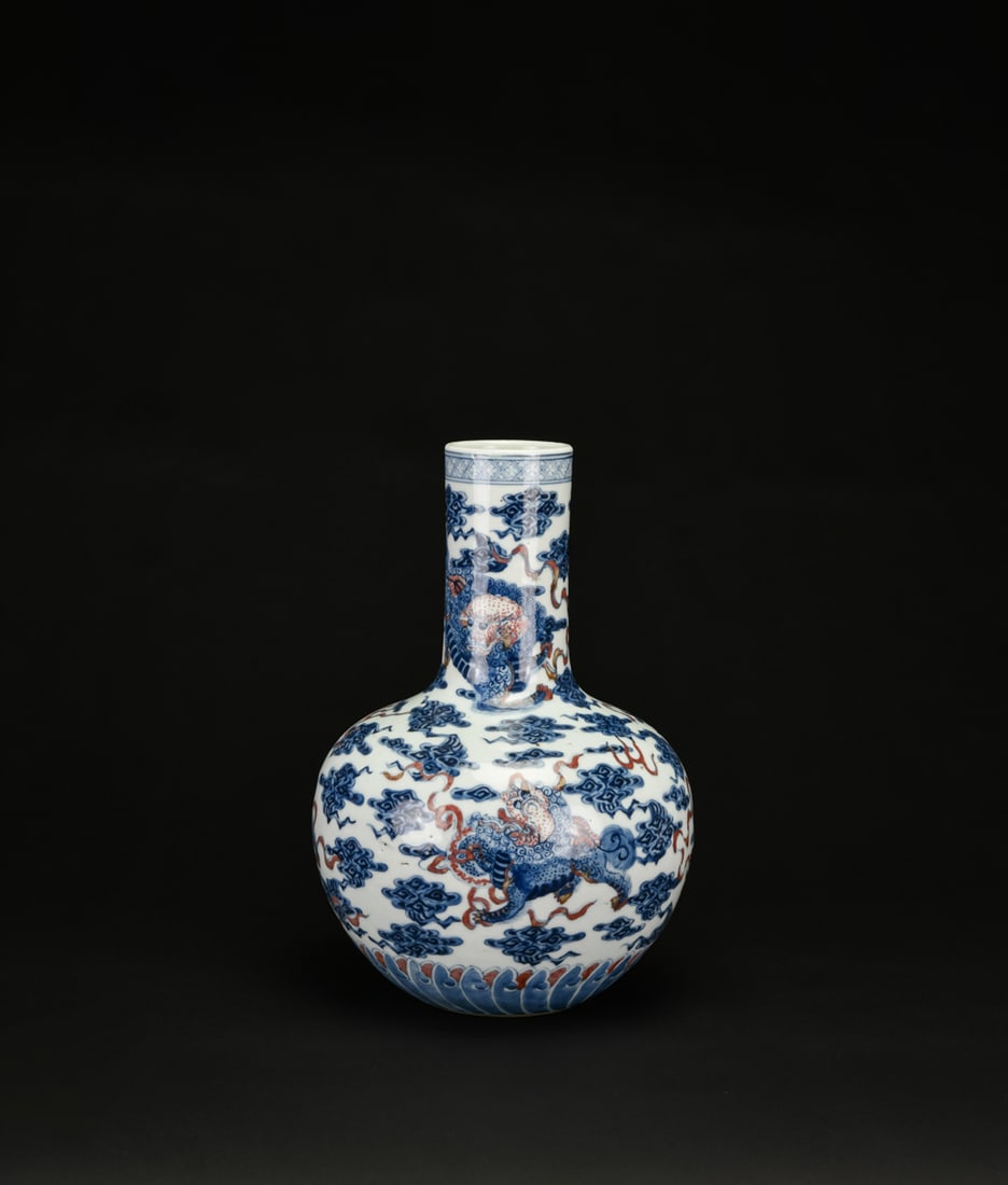 A Blue and Iron-Red ?Mythical Beast? Decorated Long-Neck Vase, Qing Dynasty: The globular body rising to a tall cylindrical neck, decorated with striding mythical beasts amid scrolling clouds in underglaze blue accented with iron-red. The base encircled by a band of stylized l