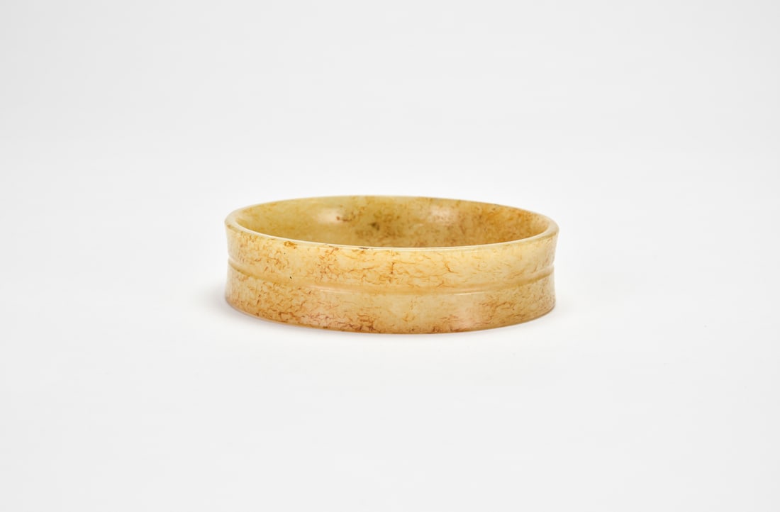 A Jade ?Xuanwen? Bracelet, Warring States Period: The jade ring is of thick-walled form with broad edges and slightly tapering sides, divided by a raised string line around the exterior. The surface is covered with yellow thread-like alteration, crea