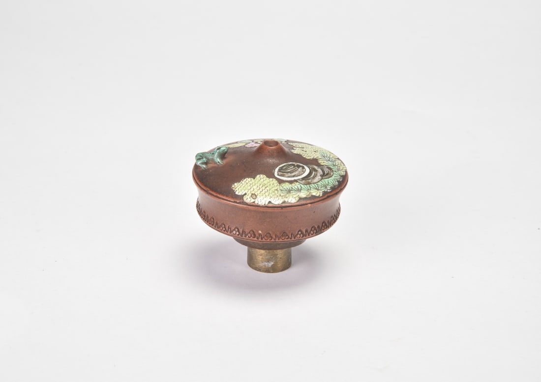 A Yixing Zisha Enameled Pine: Rock And Toad’ Smoking Vessel Fitting Of compressed circular form, the reddish-brown Yixing stoneware body is decorated in colored enamels with pine trees, rockwork and flowering and fruiting