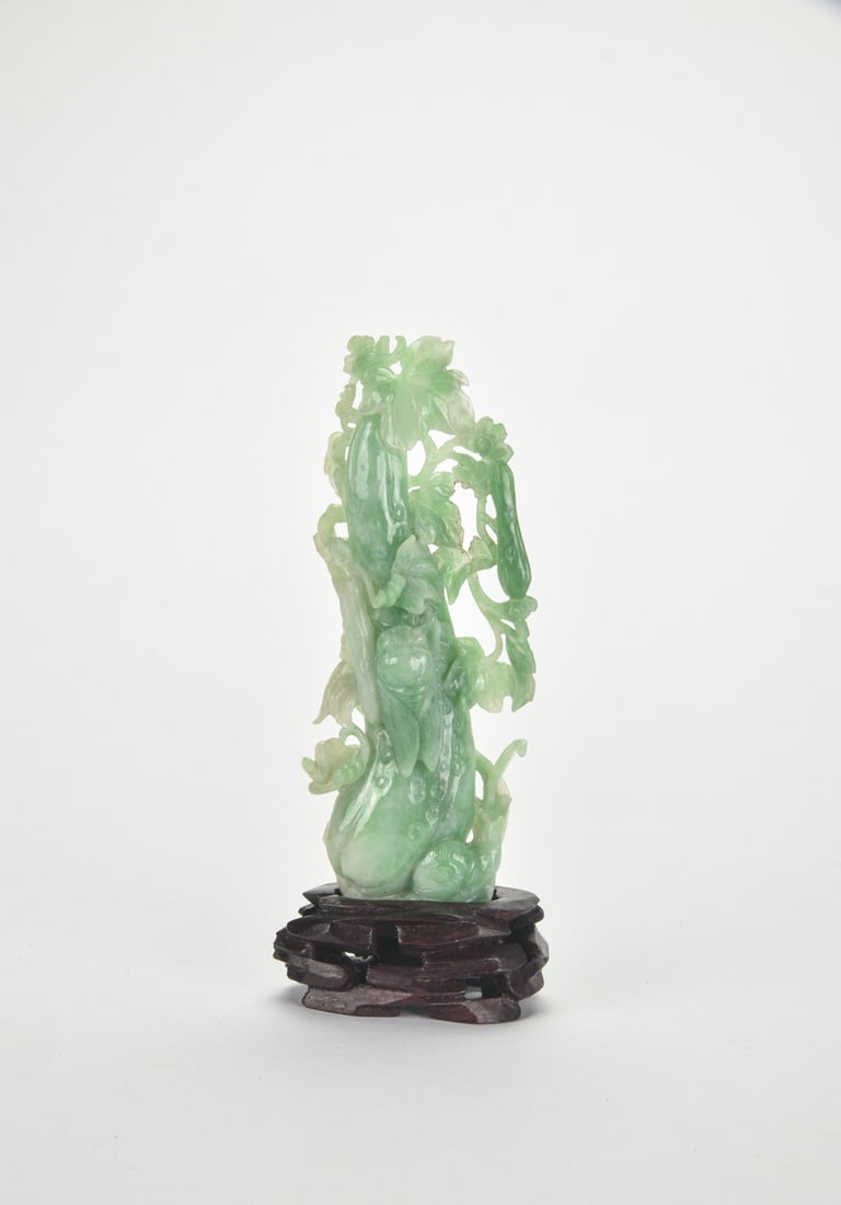 A Carved Jadeite Melons,Cicada and Snail Figure with Wood Stand.: Late Qing Dynasty–Republic Period Carved from a single piece of jadeite of pale celadon tone with emerald-green inclusions, the figure is rendered as ripened gourds borne on intertwining vines