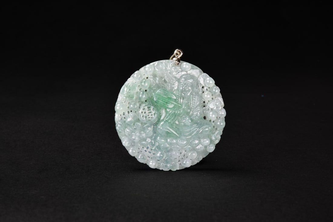 An Icy Jadeite Pendant Carved with Han Zhongli Pendant: Finely carved in high relief, the icy jadeite pendant depicts Han Zhongli, one of the Eight Daoist Immortals, holding his emblematic fan amidst clusters of grapes, peaches, lingzhi fungus, and