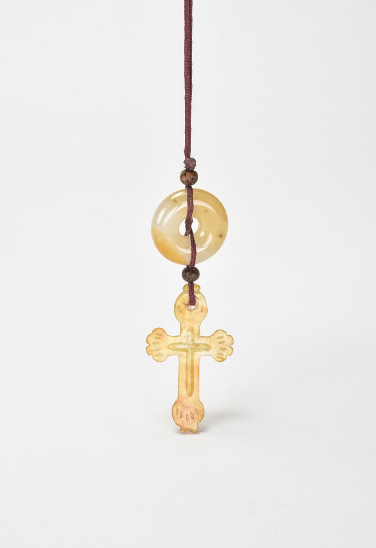 A Honey Jadeite Cross Pendant Suspended from a White Jadeite Bi Disc: Carved from translucent honey-toned jadeite of warm amber hue, the pendant is fashioned as a Latin cross with trefoil terminals in a clean, elegant form. It is suspended from a polished white jadeite 