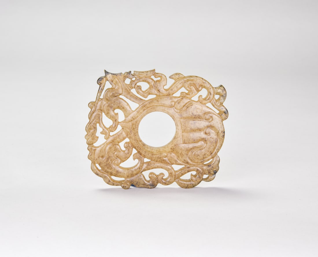Carved Jade Openwork Plaque With Dragons And Phoenixes, Han Dynasty: The pale celadon jade plaque is carved in openwork around a large central aperture, the surrounding field elaborately arranged with intertwined dragons and phoenixes. The sinuous creatures are rendere