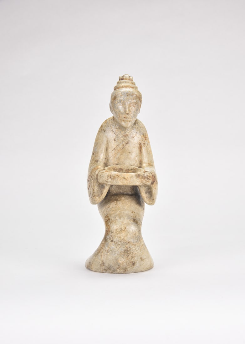 A Large Carved Jade Figure of a Kneeling Attendant, Han: The substantial jade is carved in the round as a kneeling attendant, shown with an elongated face beneath a formal headdress and dressed in a long robe with broad sleeves. The arms extend forward, wit
