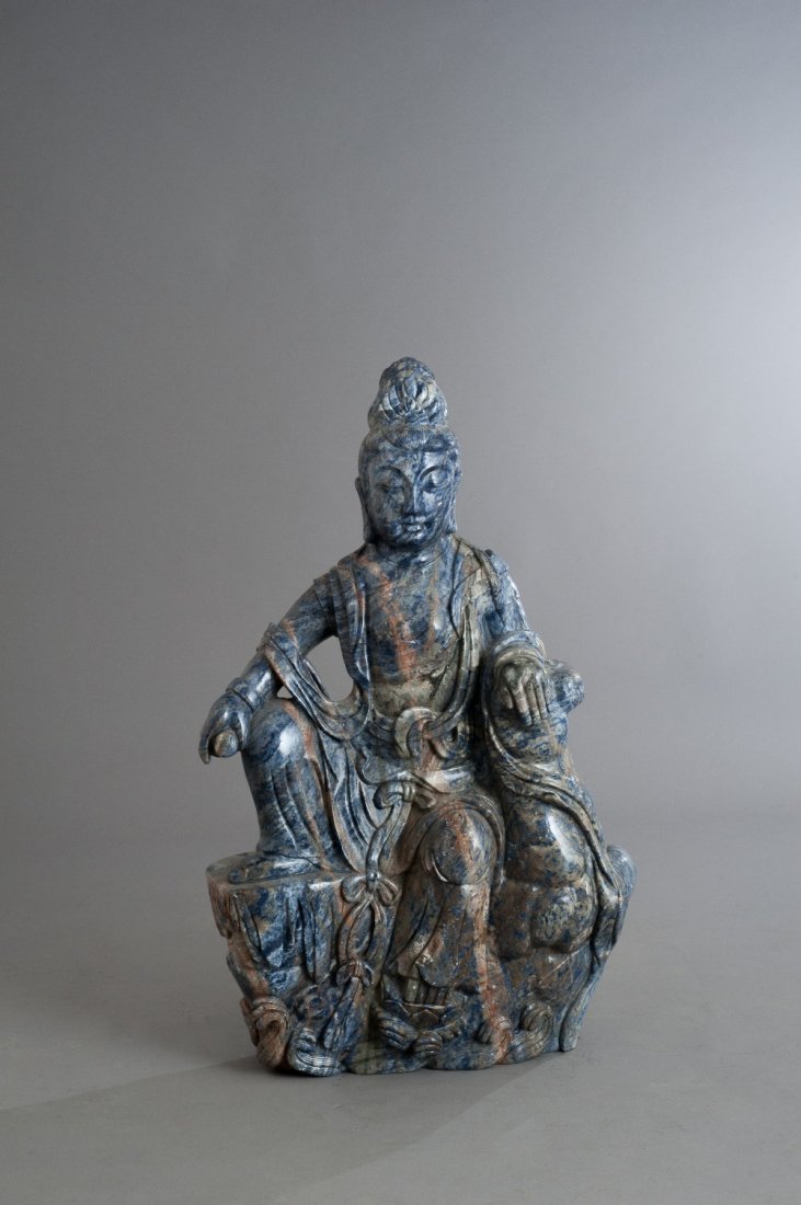 CHINA: CHINA Sculpture carved in blue veined stone of the great goddess Guanyin represented sitting on a mound. She holds a small tube in her right hand. 20th century H 33.8 in. - L 20.8 in. - W 9.44 in. H 8