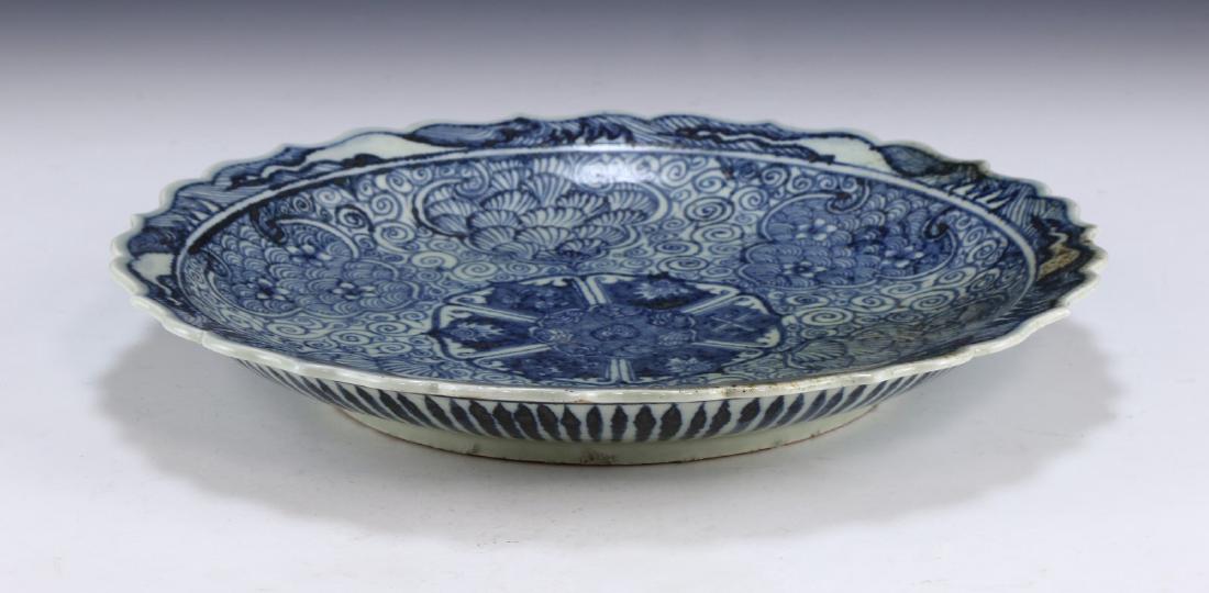 A CHINESE ANTIQUE BLUE & WHITE PORCELAIN PLATE: A Chinese Antique Blue & White Porcelain Plate: Well Potted With Scrolling Sides, Rising From A Base Rested On Low Feet To A Lipped Rim, interior Finely Painted With Sprouting Blossoms Amid Swirling G