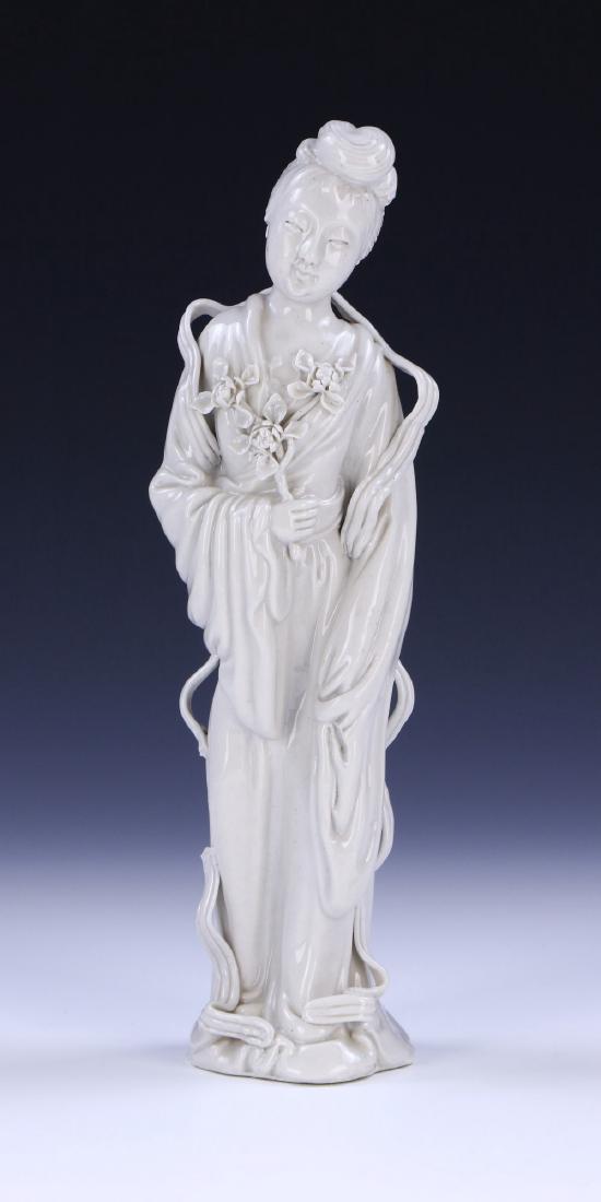 A CHINESE ANTIQUE BLANC DE CHINE PORCELAIN BEAUTY: A Chinese Antique Blanc De Chine Porcelain Beauty: Displayed in A Standing Position, Dressed in Traditional Flowing Robes, Right Hand Holding Blooming Flowers, The Porcelain Of An Even White Tone; Siz